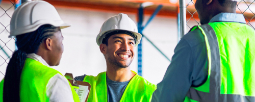 Tre lavoratori sorridenti in gilet di sicurezza ed elmetti in un magazzino Tre lavoratori sorridenti in gilet di sicurezza ed elmetti in un magazzino